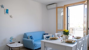 Een moderne woonkamer met een blauwe bank, een witte eettafel gedekt voor twee personen, en een bijzettafeltje met decoratieve objecten.