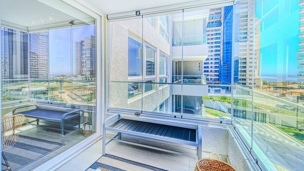 Ein moderner Balkon mit Glasgeländern, einer Bank und einem Korbwäscher.