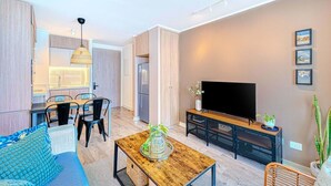 Ein modernes Wohnzimmer mit Sofa, Couchtisch, Fernseher und einem Essbereich mit Stühlen und Tisch.