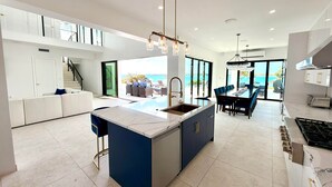 A modern kitchen with a central island, a dining area with a view, and a staircase leading to a balcony. - Vantage Point Exuma Ultra-Luxury Villa - Heated Pool & Golf Cart (Rokers Point Settlement)