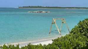 Ein Strand mit klarem türkisfarbenem Wasser, einer Holzschaukel und einer fernen Insel.