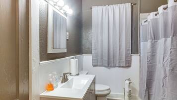 A bathroom with a sink, mirror, toilet, and shower curtain.