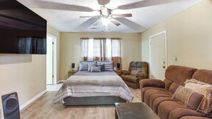 A bedroom with a bed, a ceiling fan, a window with curtains, a door, and a brown couch. - Cozy Vicksburg Home w/ Patio ~ 1 Mi to Riverfront! (Vicksburg)