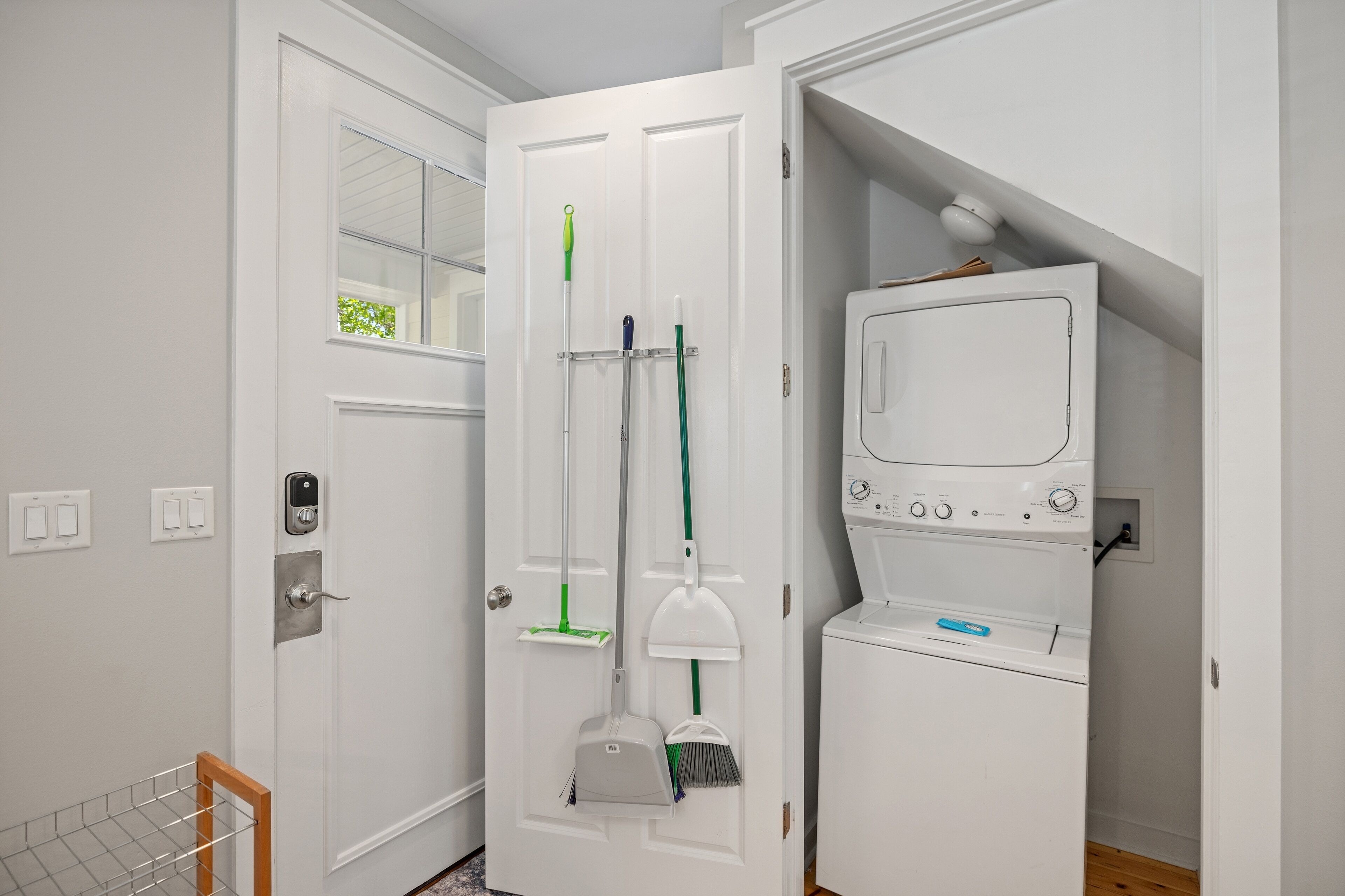 A laundry room with a white washing machine, a drying rack, and various cleaning tools.