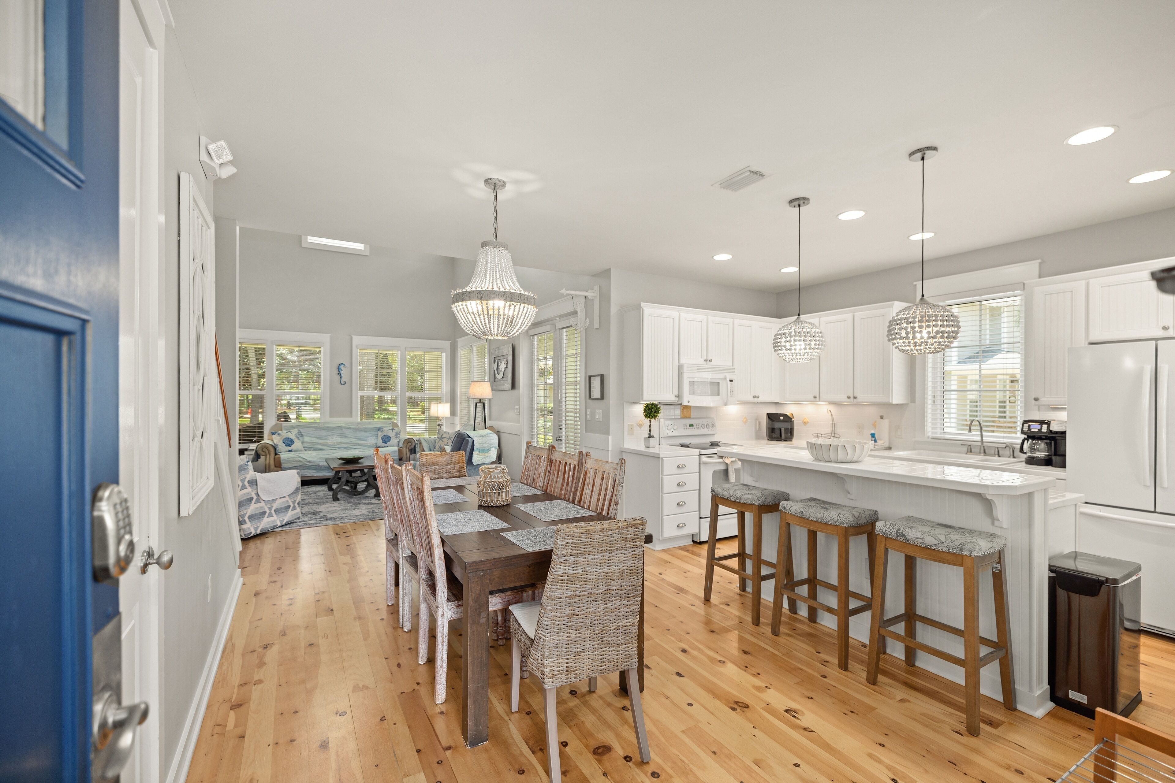 A modern kitchen with white cabinets, a wooden dining table with wicker chairs, and pendant lights.