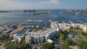 A marina with multiple docks and boats, a large hotel with a modern design, and a coastal cityscape in the background. - The Moorings 103 3 Bedroom Condo by RedAwning (Orange Beach)