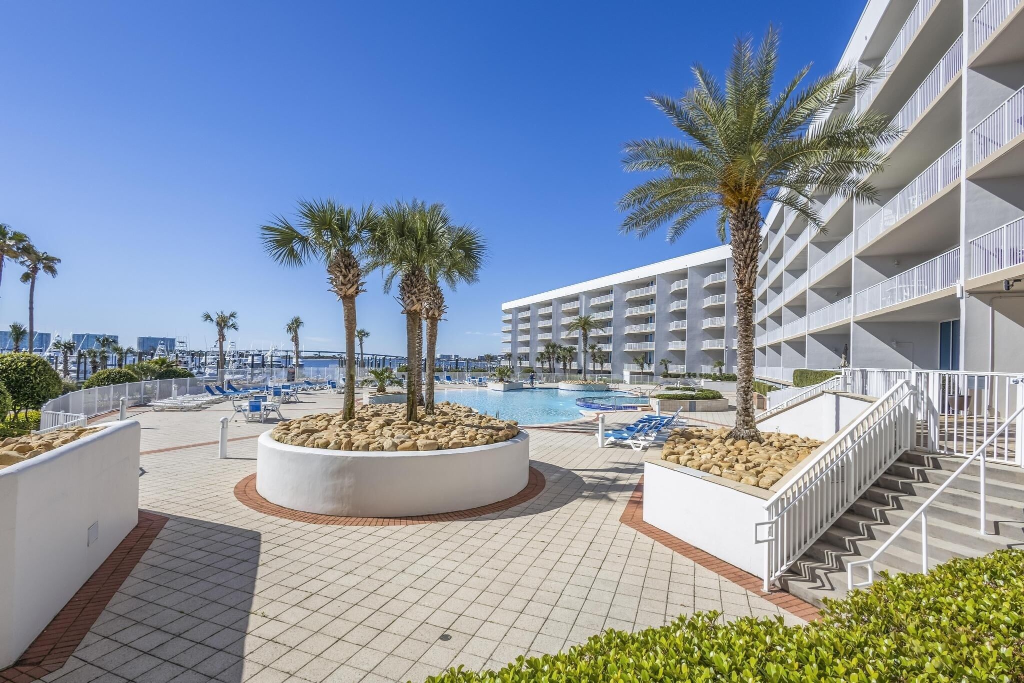 A resort pool area with palm trees, lounge chairs, and a modern building with balconies.