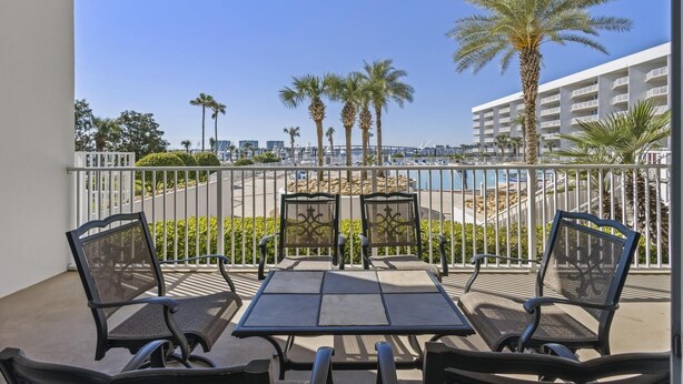 A balcony with two tables and four chairs, overlooking a beach and a marina. - The Moorings 103 3 Bedroom Condo by RedAwning (Orange Beach)