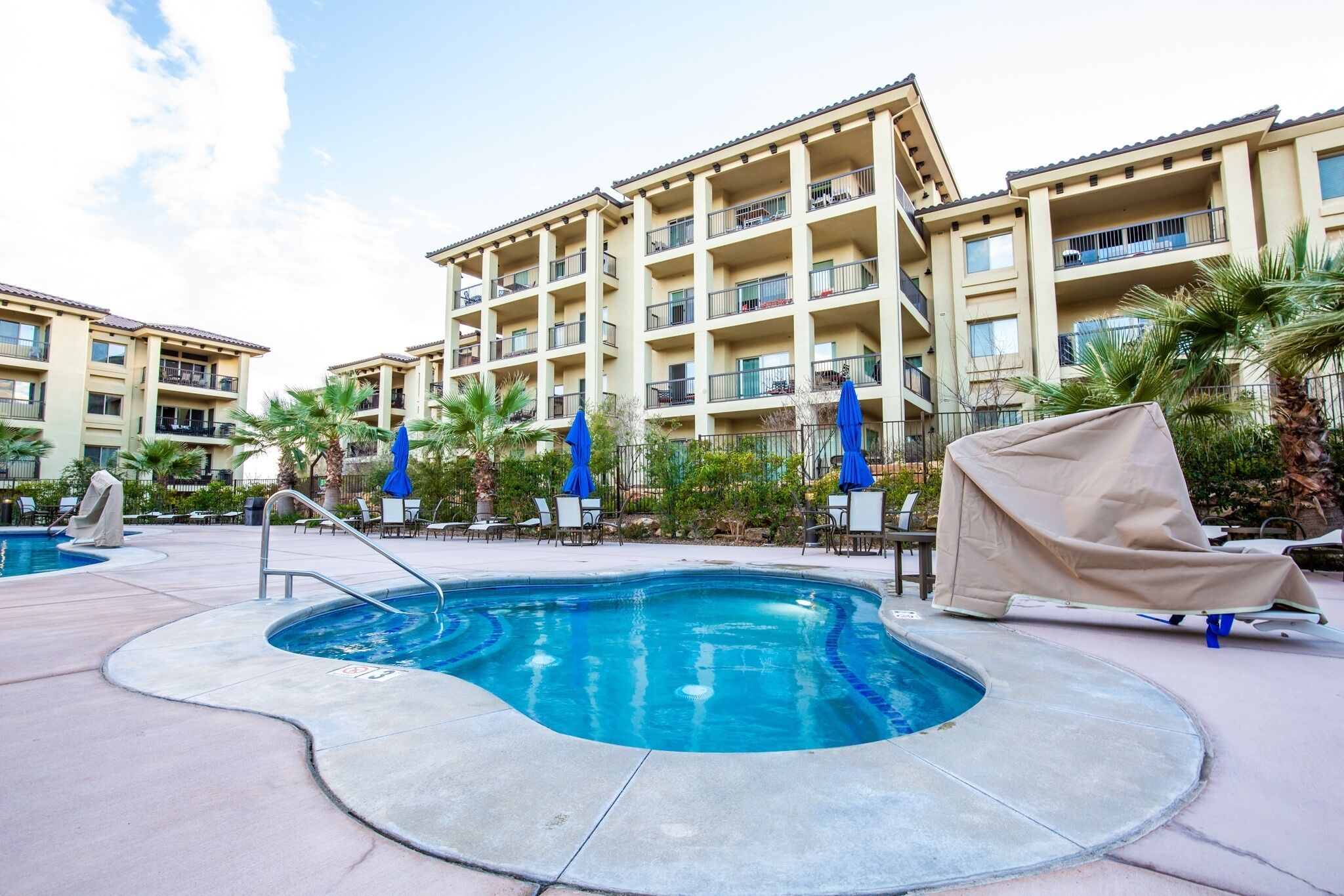 A swimming pool with a poolside area, lounge chairs, and umbrellas.