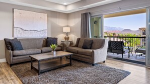 A modern living room with two sofas, a coffee table, and a lamp. There is a large window with a view of mountains and a balcony with outdoor furniture. - Sunset Point #w302 3 Bedroom Condo (St. George)