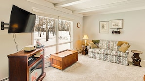 A living room with a television, a wooden cabinet, a sofa, and a window with a view of trees. - Family-friendly Home w/ Fire Pit in Pine River (Pine River)