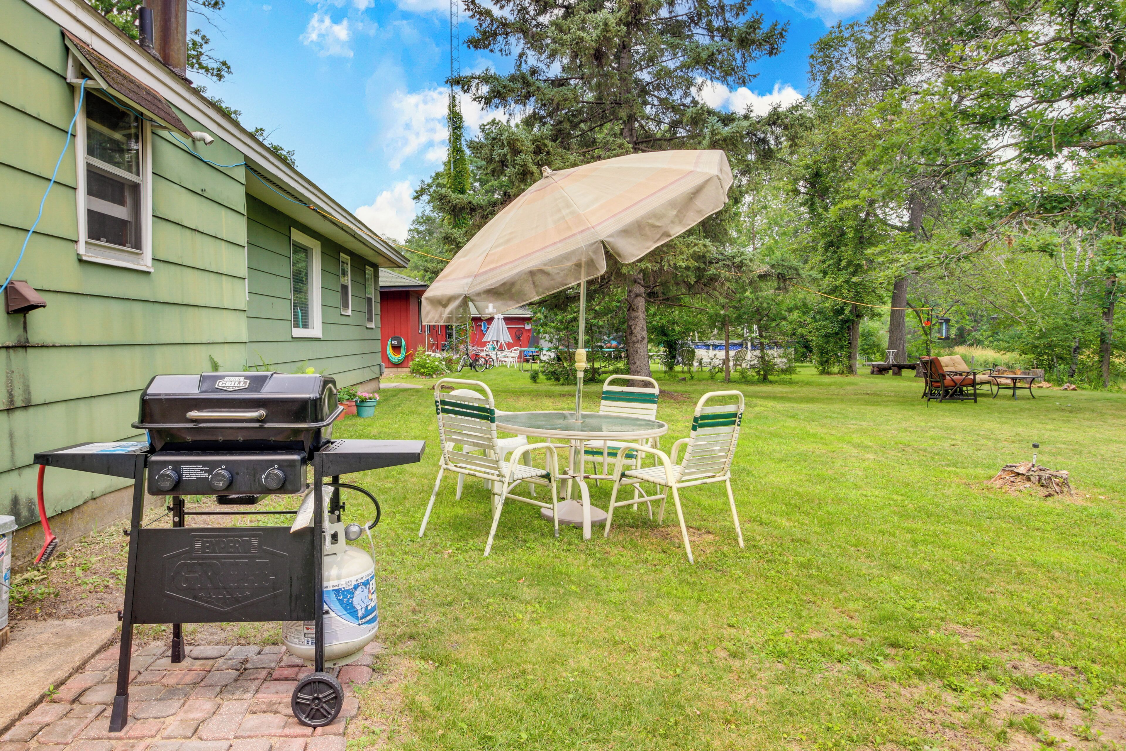 A backyard with a grill, a table with chairs, and a covered umbrella.