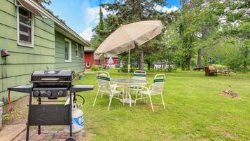 A backyard with a grill, a table with chairs, and a covered umbrella.