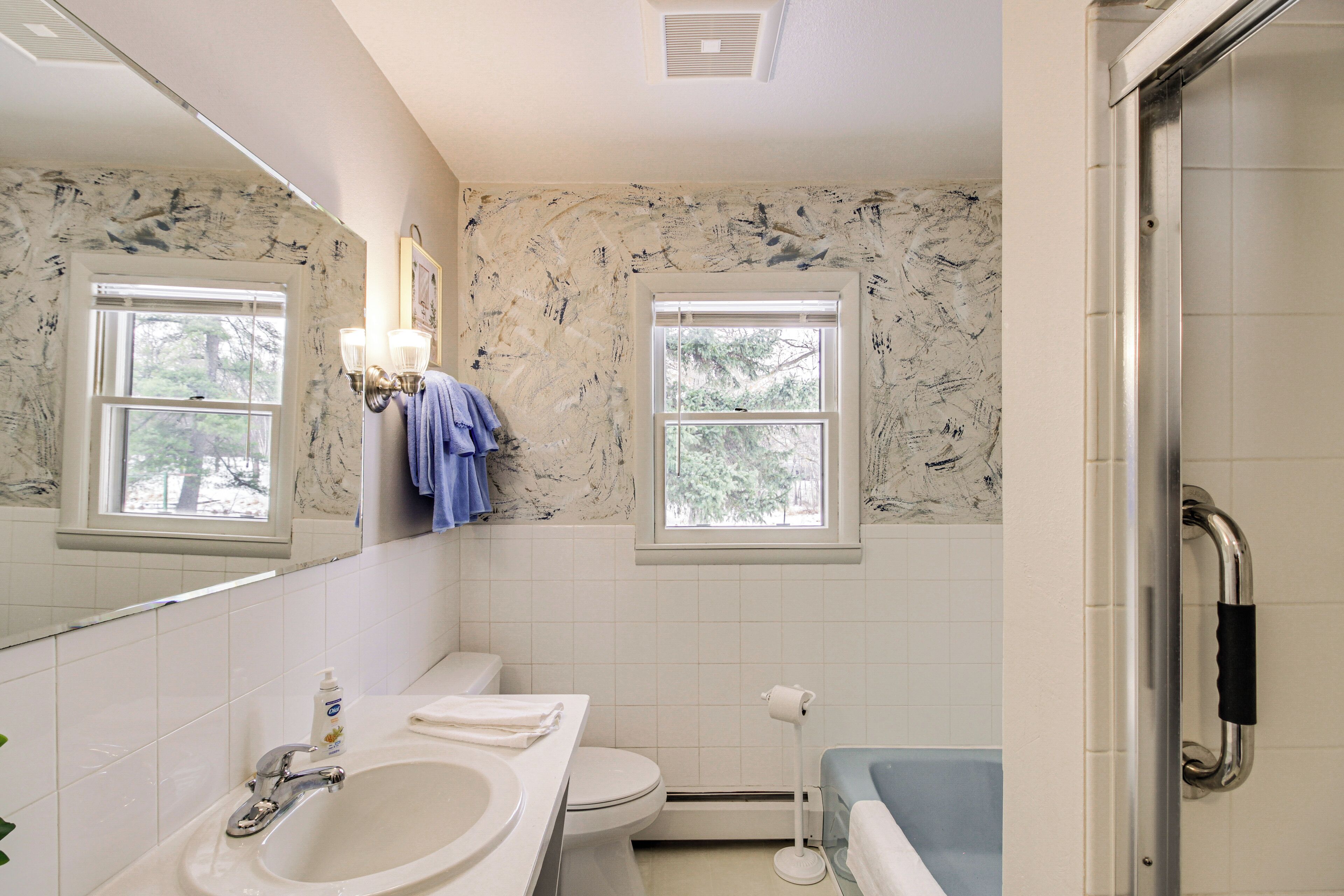 A bathroom with a sink, toilet, and bathtub. There are two windows and a mirror.