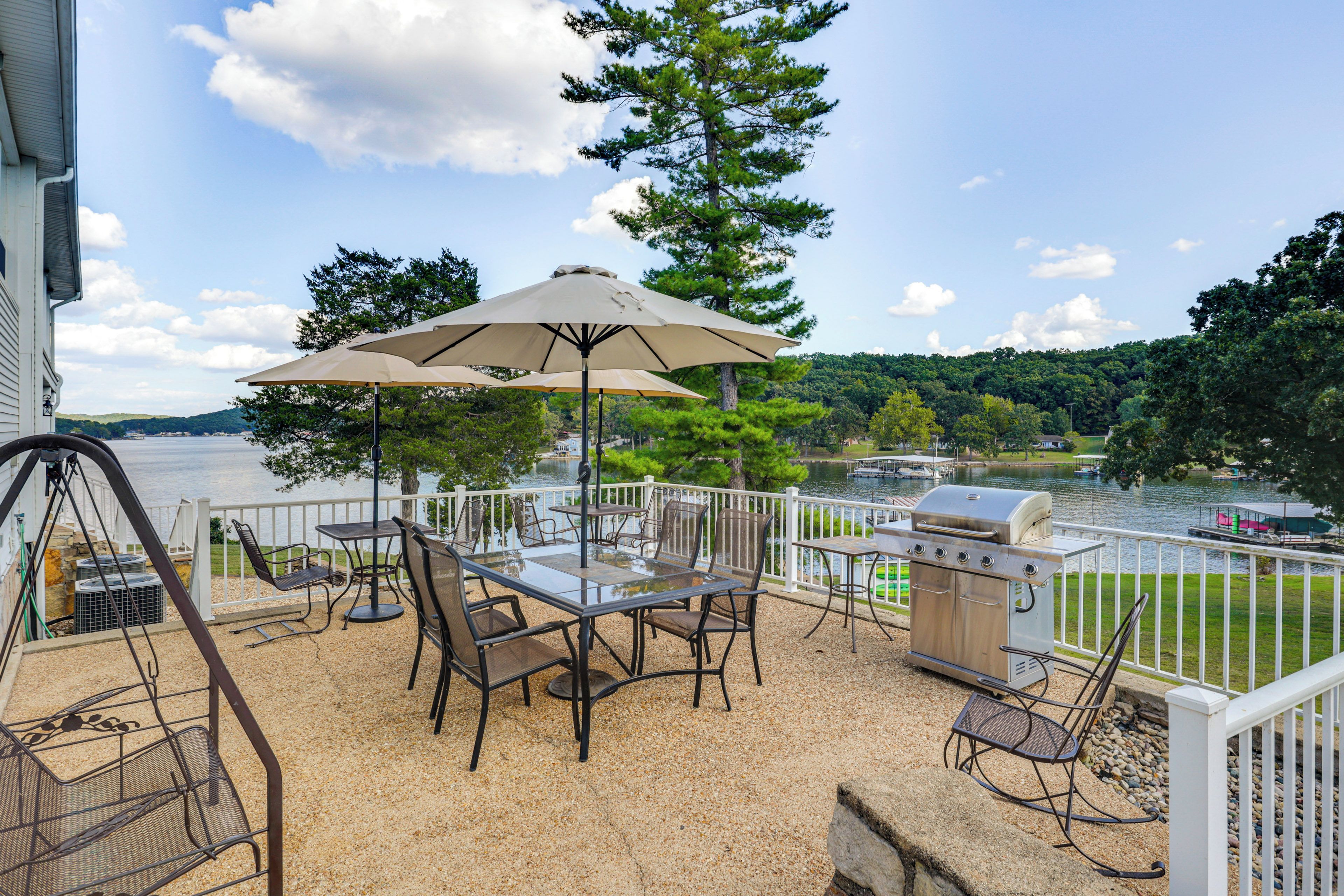 An outdoor patio with a table and chairs, a grill, and a view of a lake.