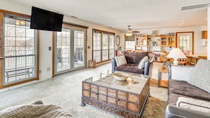 A spacious living room with a large window, a flat-screen TV, a coffee table, and a fireplace. - Private Dock & Ozarks Shoreline: 5BR Lake House (Roach)