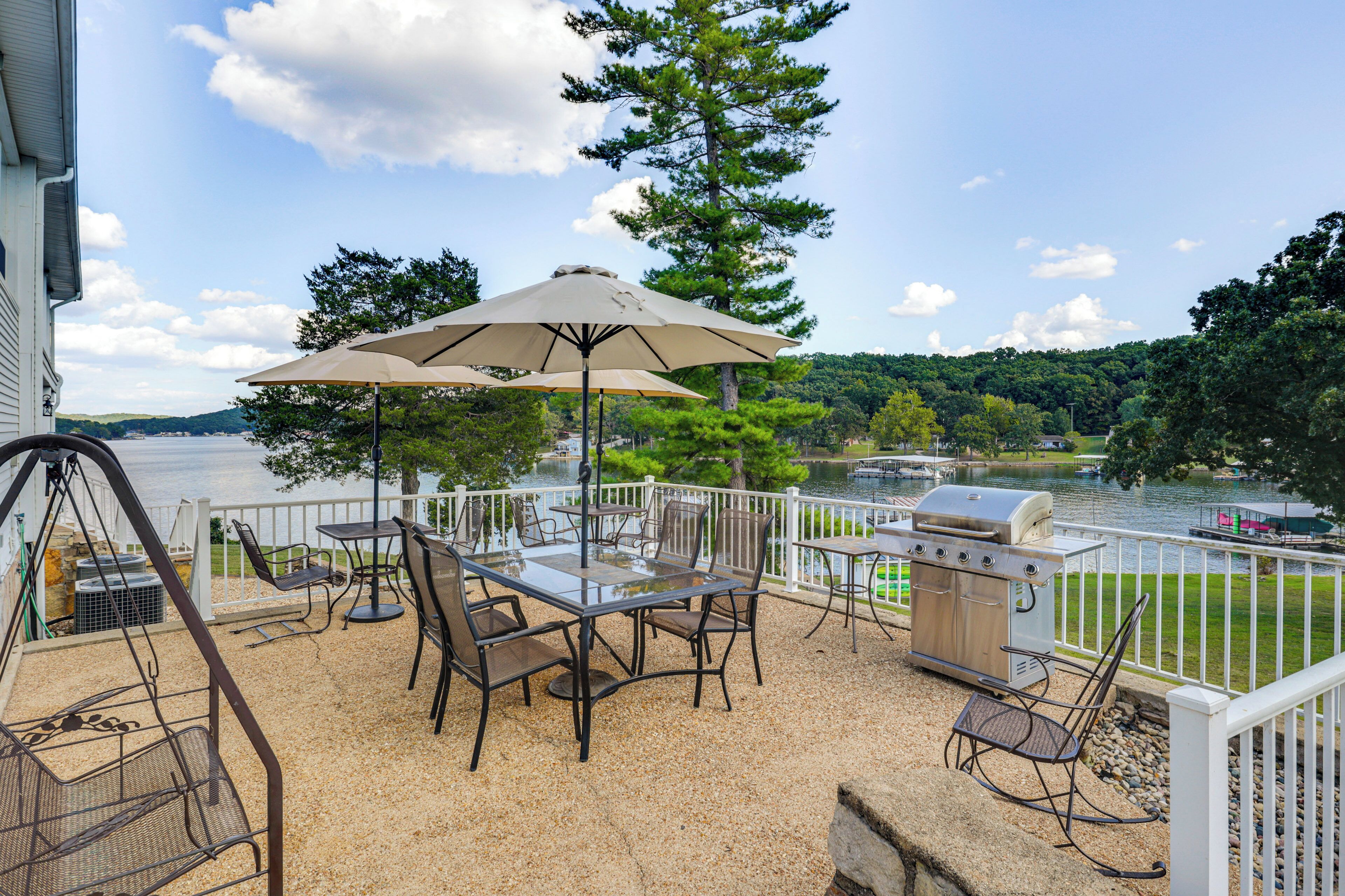 An outdoor patio with a table and chairs, a grill, and a view of a lake.