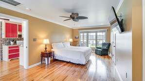 A bedroom with a bed, a ceiling fan, a TV, and a view of the outside.