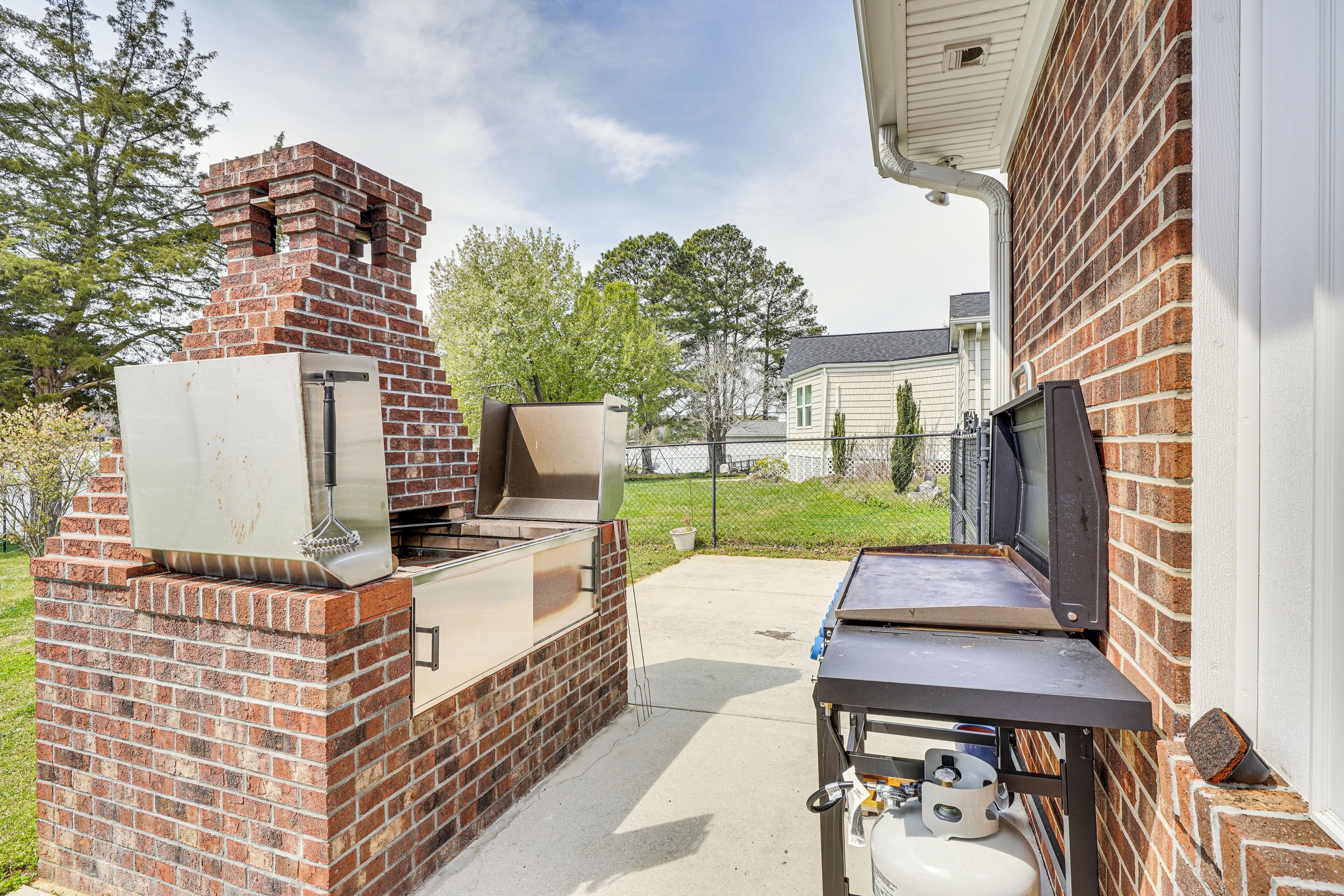 Un espace barbecue extérieur en briques, équipé d’une bouteille de gaz et d’un téléviseur posé sur un meuble.