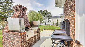 Un espace barbecue extérieur en briques, équipé d’une bouteille de gaz et d’un téléviseur posé sur un meuble.