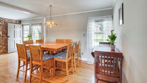 A dining area with a wooden table and chairs, a hanging light fixture, and a view of the outdoors through large windows.