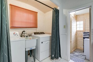 A compact bathroom with a washing machine, sink, and shower curtain. - Downtown Anaconda Studio: Walk to Dining & Bars! (Anaconda)