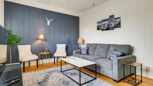 En stue med en grå sofa, to hvide lænestole, et sofabord, et sofabord og et monteret dådyrhoved.