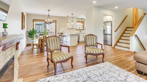 A spacious living room with wooden flooring, a fireplace, and a dining area with striped chairs. - Forest-view Deck & Fire Pit: Poconos Escape! (East Stroudsburg)