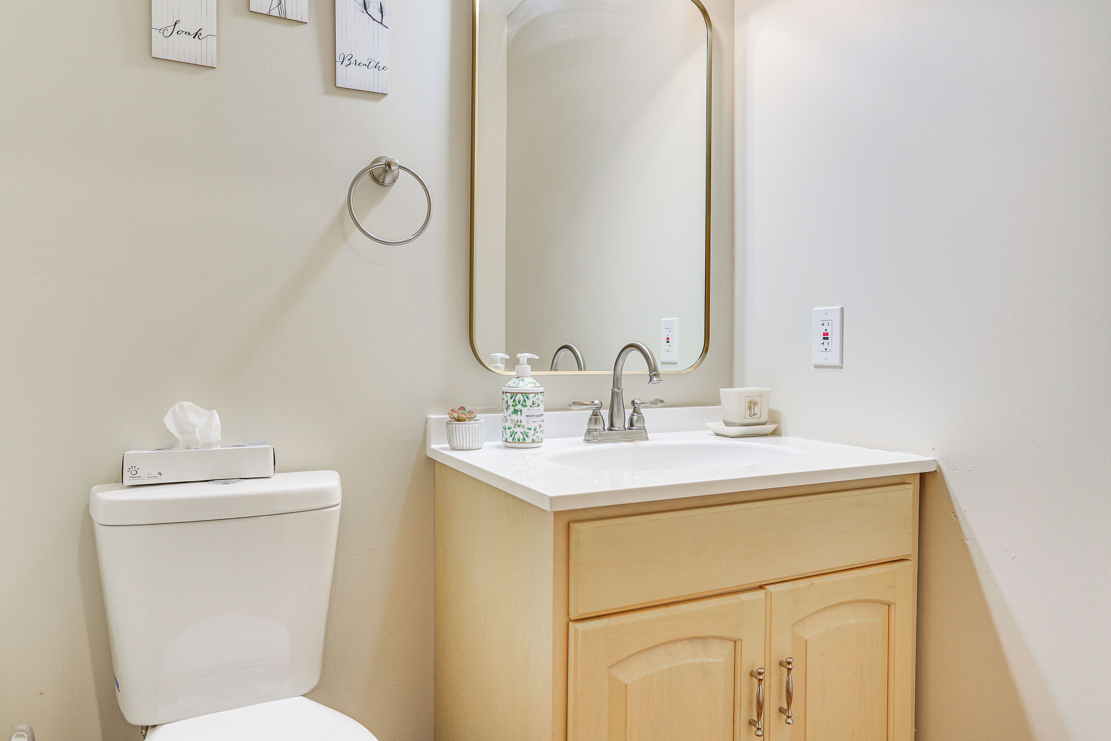 A bathroom with a toilet, sink, mirror, and wooden cabinets.