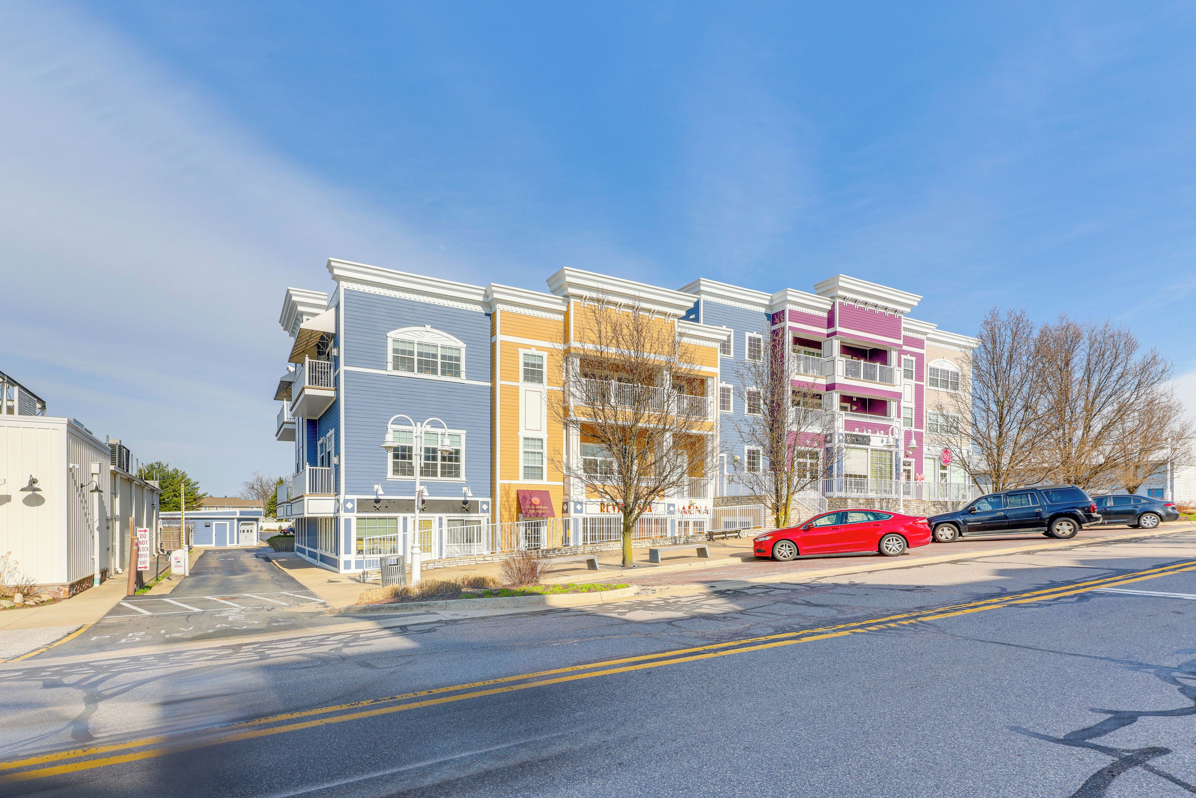 A multi-story residential building with balconies, a parking area, and a clear sky.