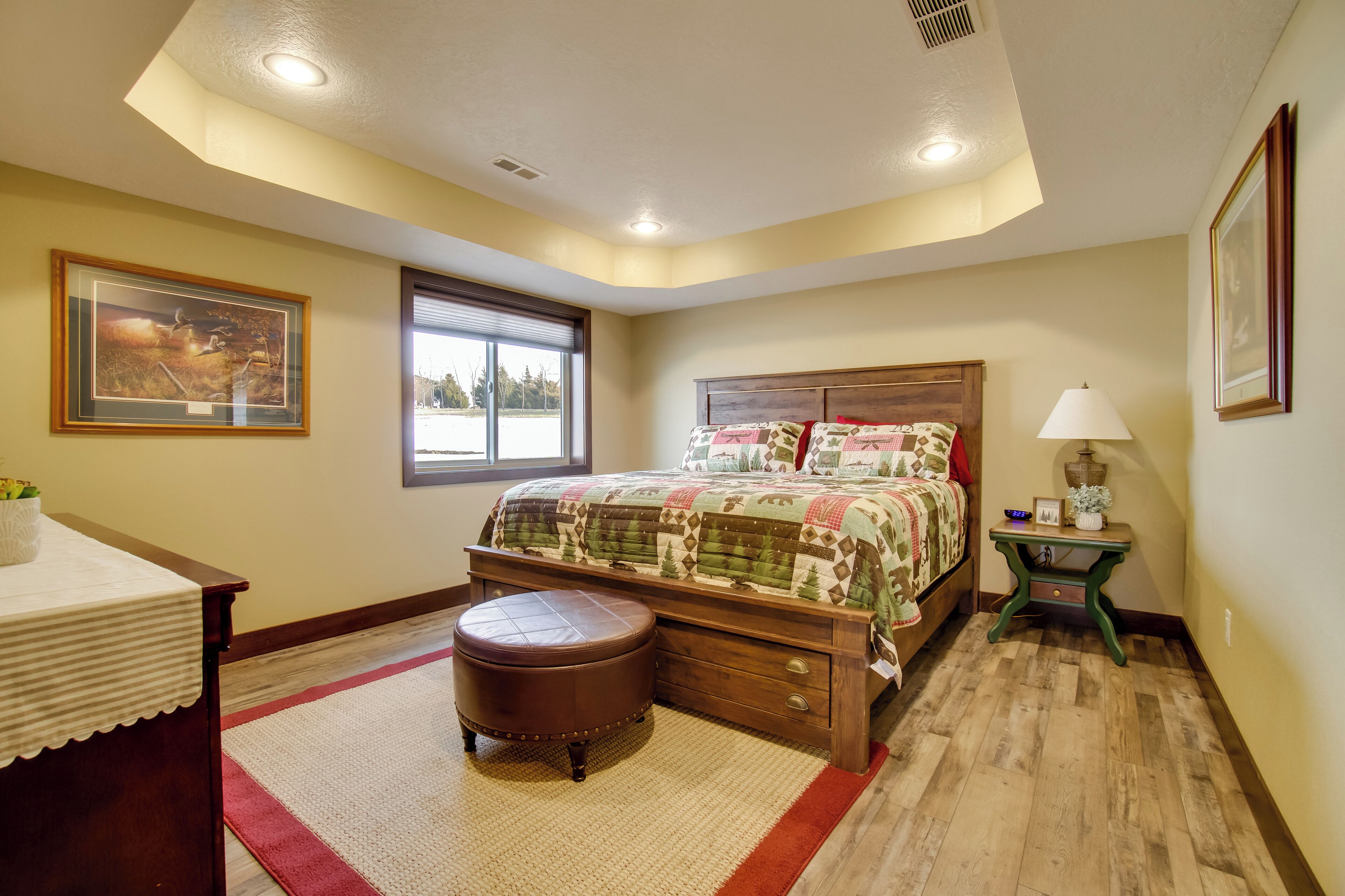 A bedroom with a large bed, a wooden nightstand, a small table, and a window with blinds.
