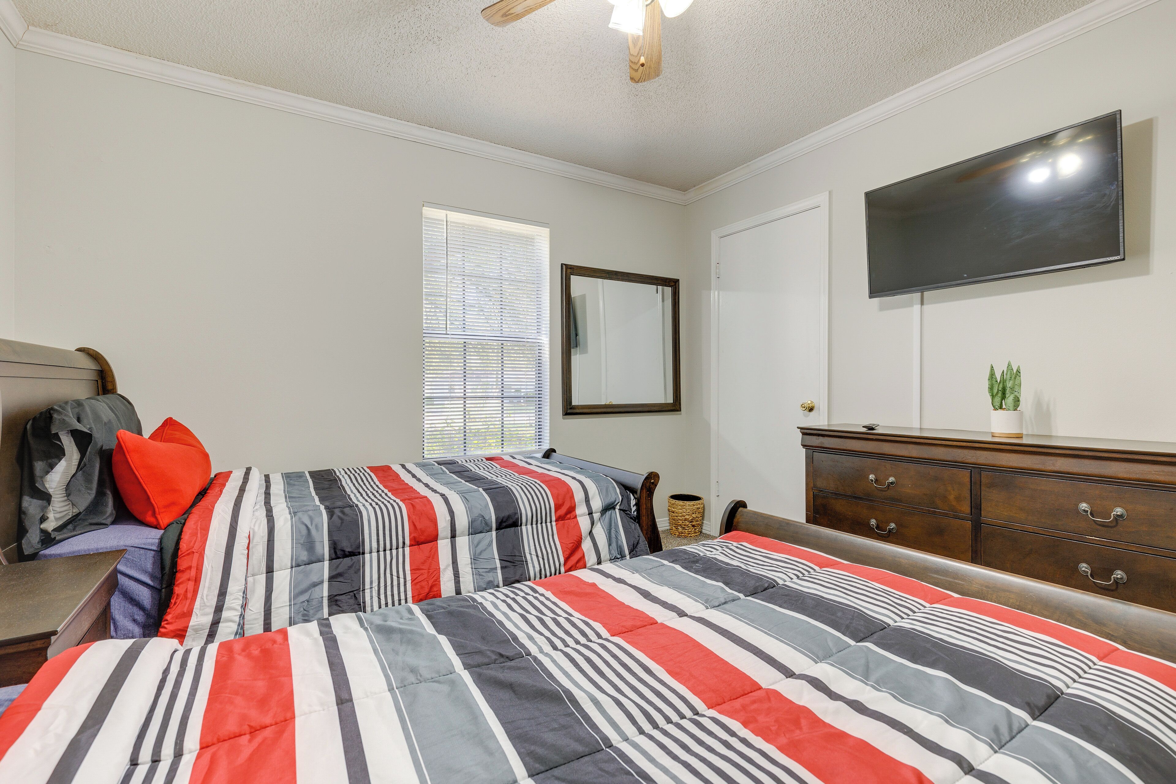 A bedroom with two beds, a dresser, a TV, and a window with blinds.