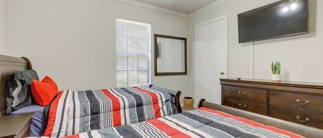 A bedroom with two beds, a dresser, a TV, and a window with blinds.