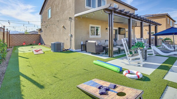 A backyard with artificial grass, a wooden table, outdoor furniture, and a pergola.