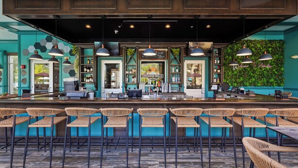 A bar area with a counter, bar stools, and a green wall with a sign.