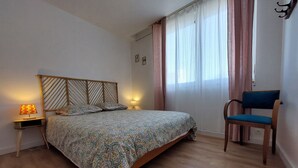 Un dormitorio con cama de madera, una mesita de noche con lámpara, una silla y una ventana con cortinas.