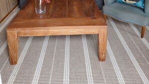 Una sala de estar con un sofá gris, un sillón azul, una mesa de centro de madera y un jarrón con flores.