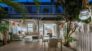 Ein Terrassenbereich im Freien mit Holzboden, einer Sitzecke mit Sofa und Sesseln sowie Blick auf das Haus im Hintergrund.