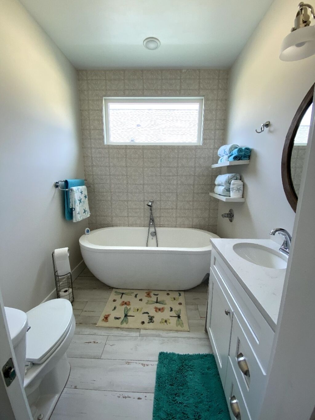 A compact bathroom with a freestanding bathtub, a toilet, a sink, and a window providing natural light.
