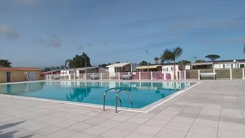 Una piscina con borde de baldosas, rodeada de casas móviles con valla.
