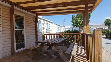 Eine Holzterrasse mit Picknicktisch und überdachtem Bereich, angrenzend an ein Haus mit einer Schiebeglastür.