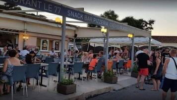 Ein Außenbereich mit Tischen und Stühlen, ein überdachter Sitzbereich und ein Schild für eine Snackbar und Pizzeria.