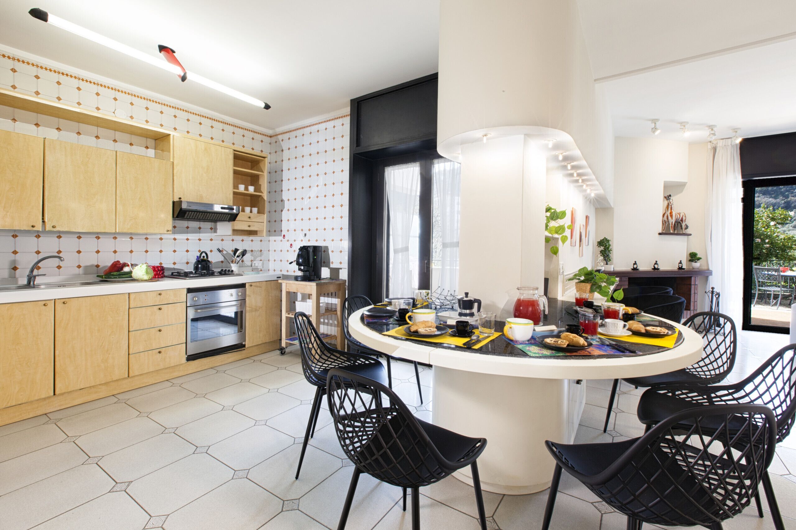 Une cuisine moderne avec des meubles en bois, un îlot central doté de chaises et un coin repas offrant une vue sur l’extérieur.
