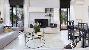 A modern living room with a sofa, coffee table, TV, and dining area. - Estate4home - Maison Wally (Sorrento)