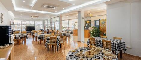 Uma sala de jantar ampla com toalhas de mesa xadrez, cadeiras de madeira e diversos pratos dispostos sobre as mesas.
