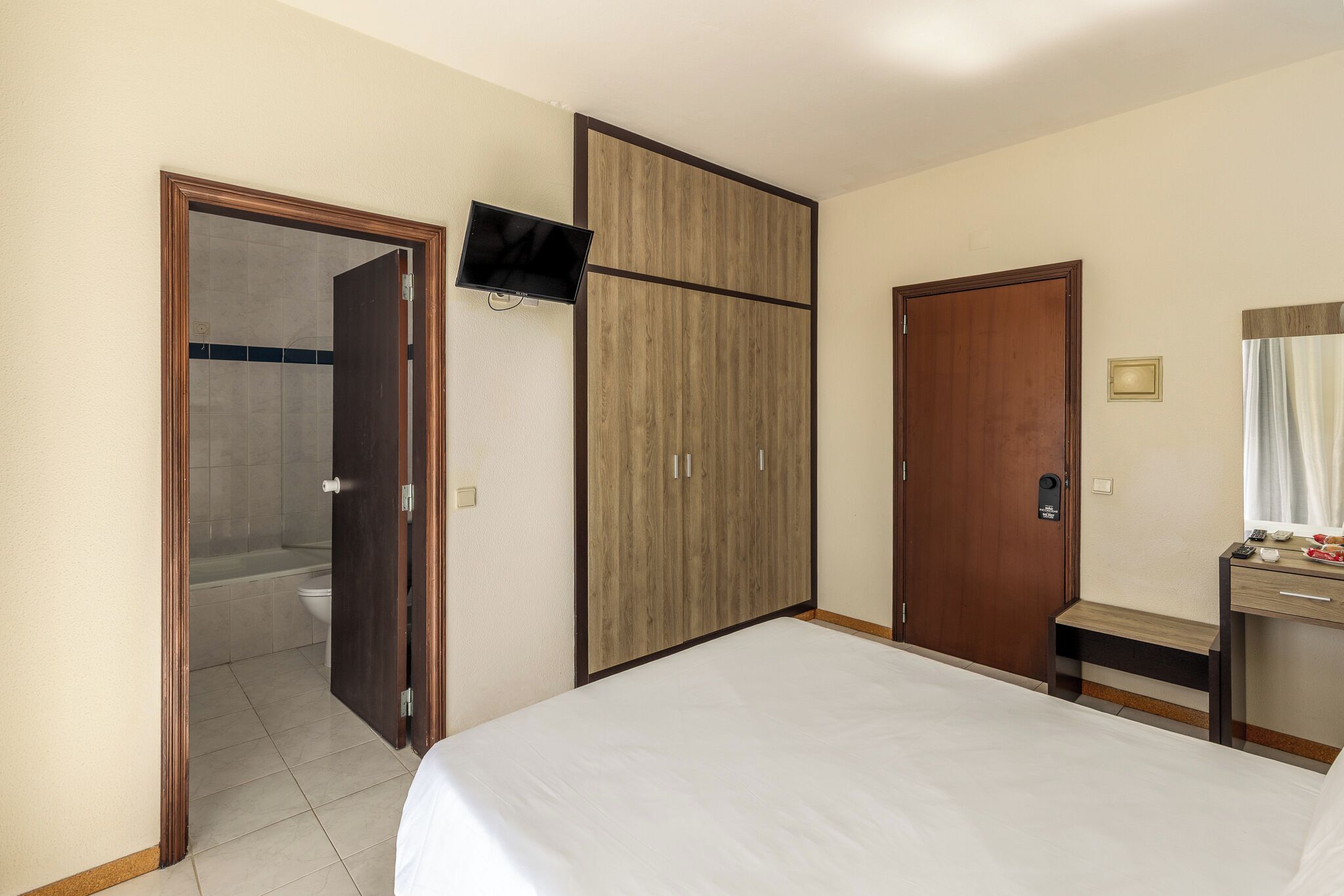 Habitació d'hotel amb un llit, un armari de fusta, una televisió, un bany amb dutxa i un escriptori amb mirall.