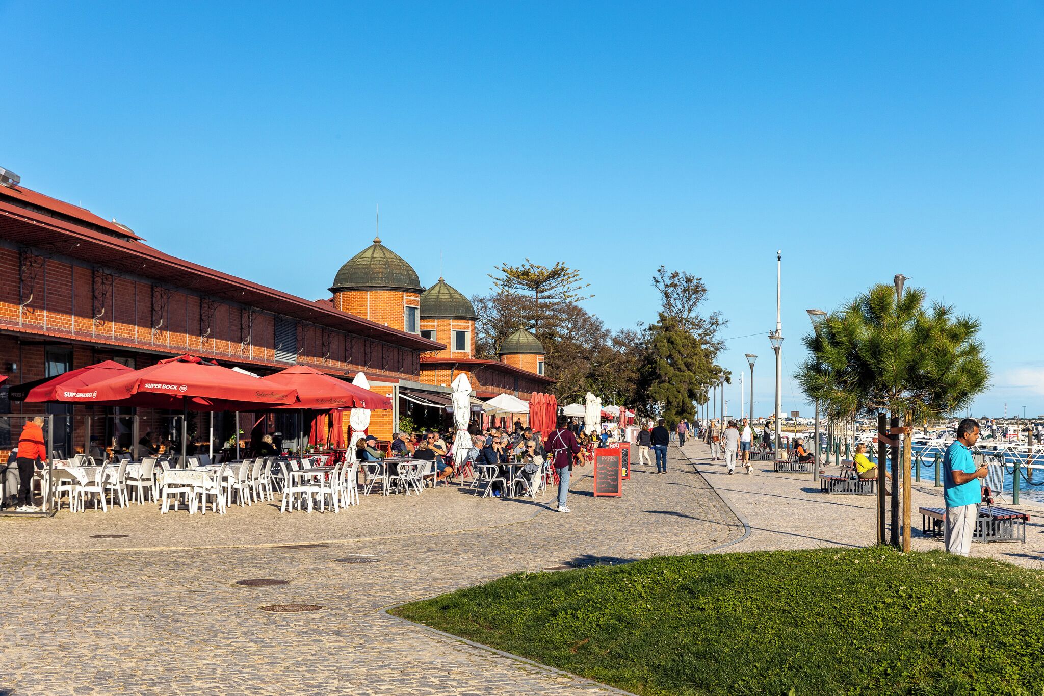 Ett offentligt torg med utomhusservering, en byggnad med kupolformad arkitektur och en klar himmel.