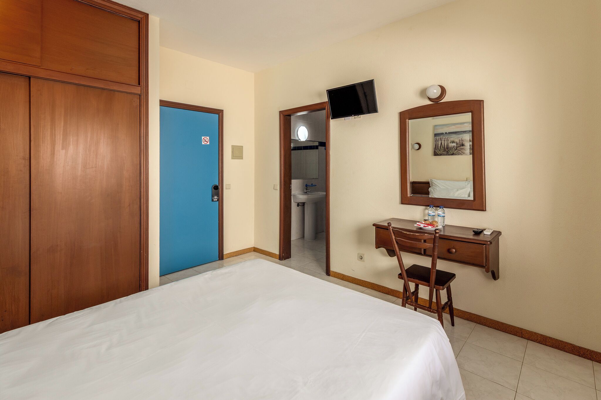 Habitació d'hotel amb llit, escriptori amb cadira, televisió i porta.