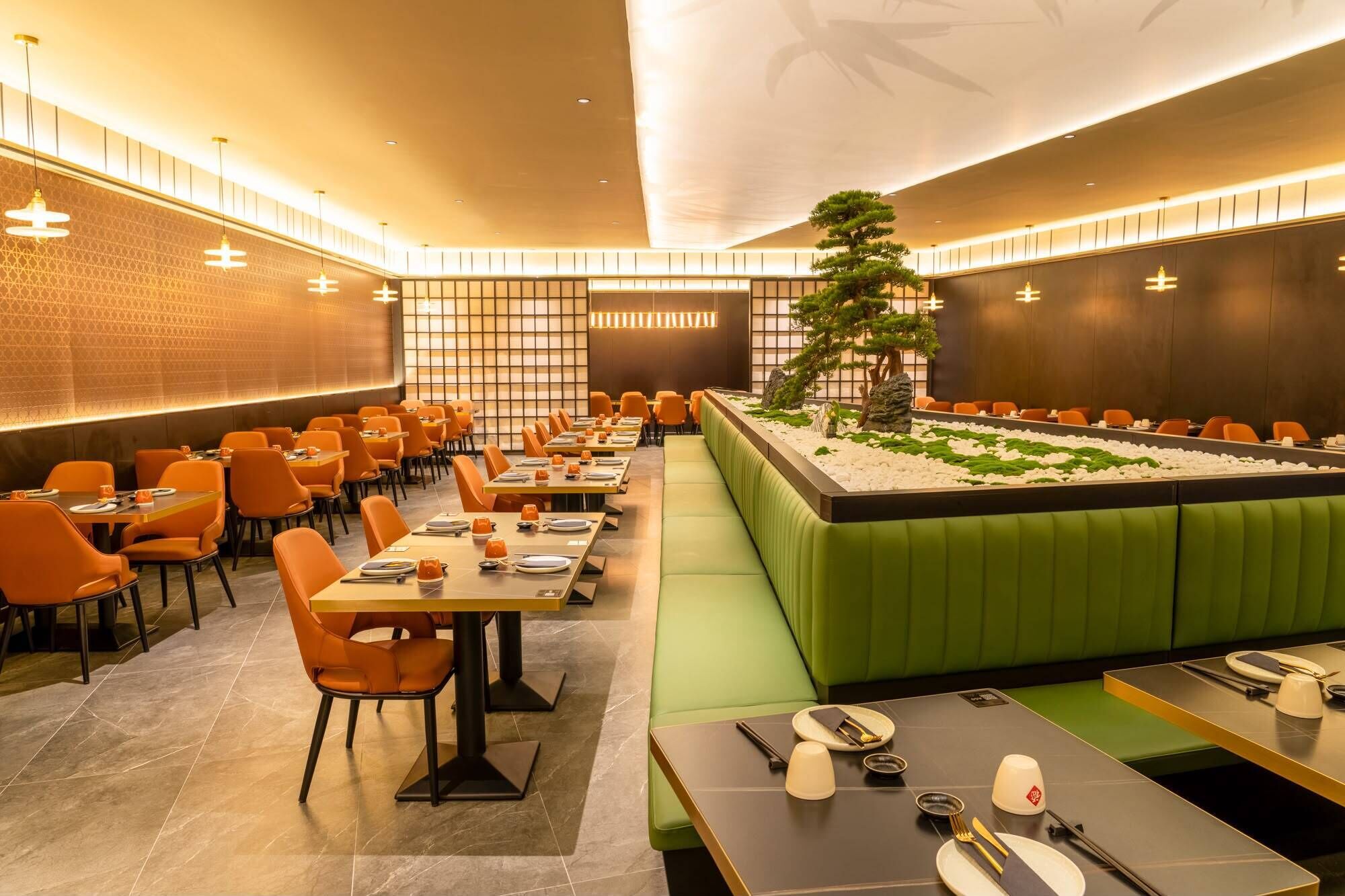 A restaurant with a long dining table, orange chairs, and a green booth area.