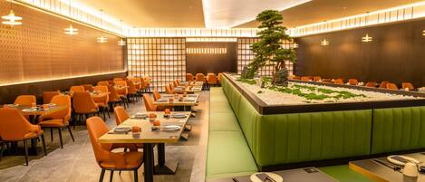 Ein Restaurant mit einem langen Esstisch, orangefarbenen Stühlen und einer grünen Sitzecke.